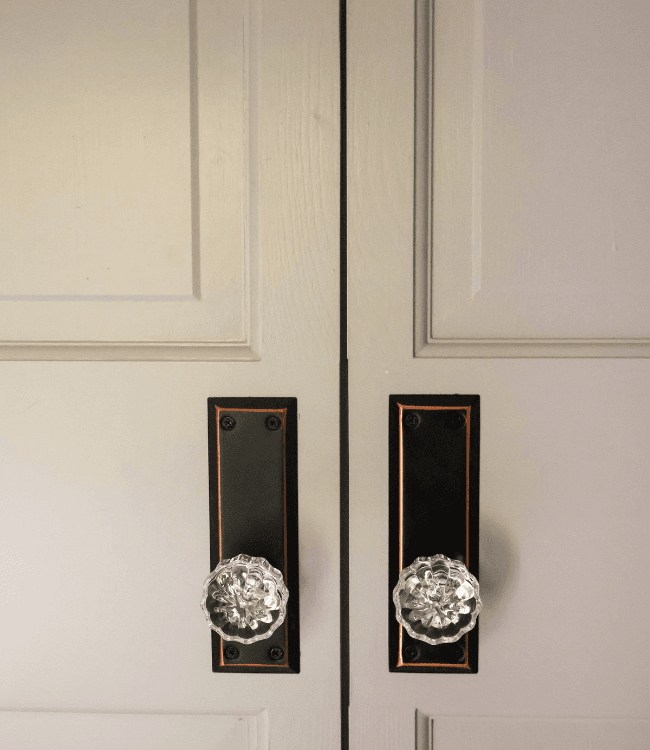 A close-up of two decorative door handles on a pair of light grey doors.