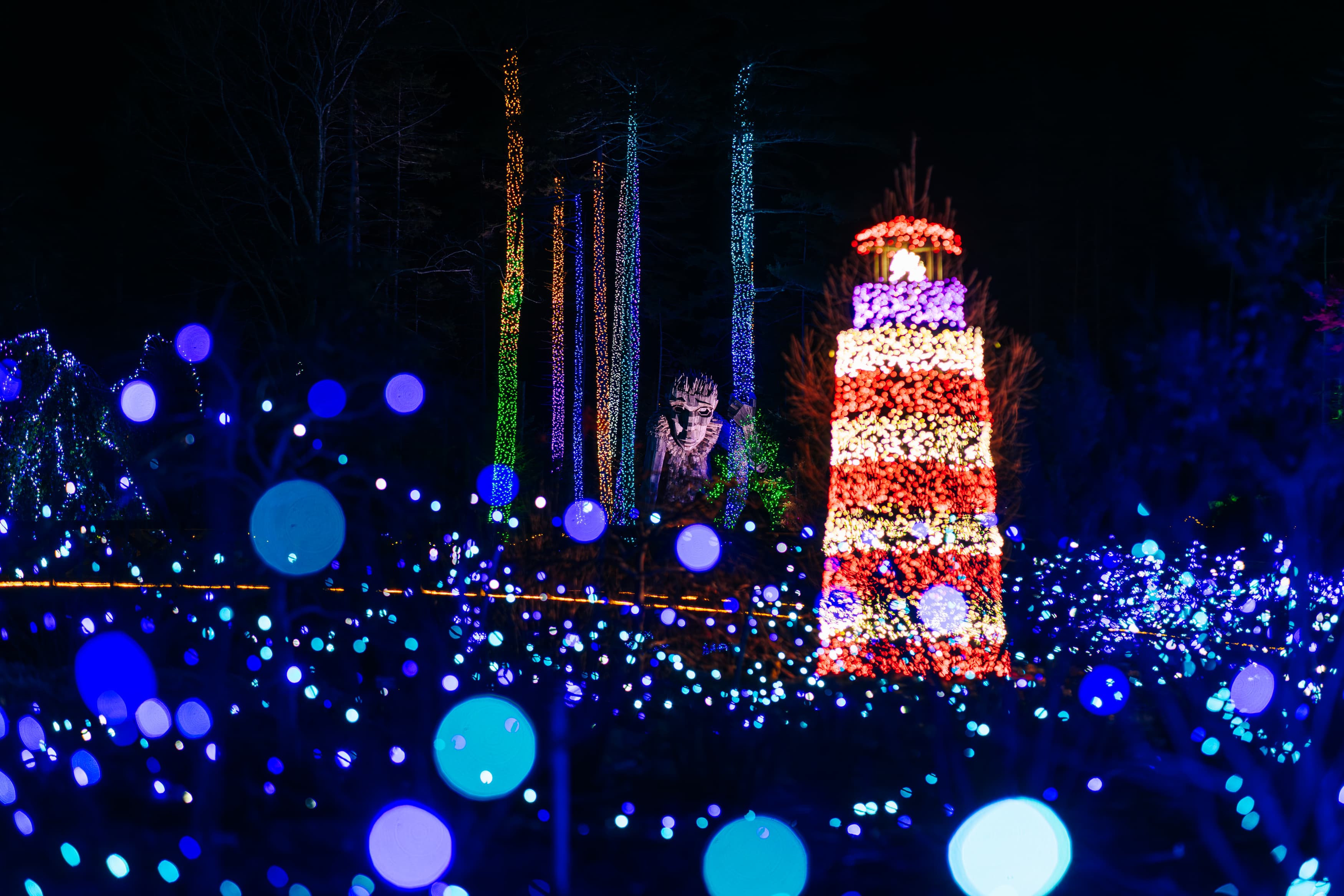 A colorful display of holiday lights featuring a lighthouse and abstract shapes in blue and purple hues.