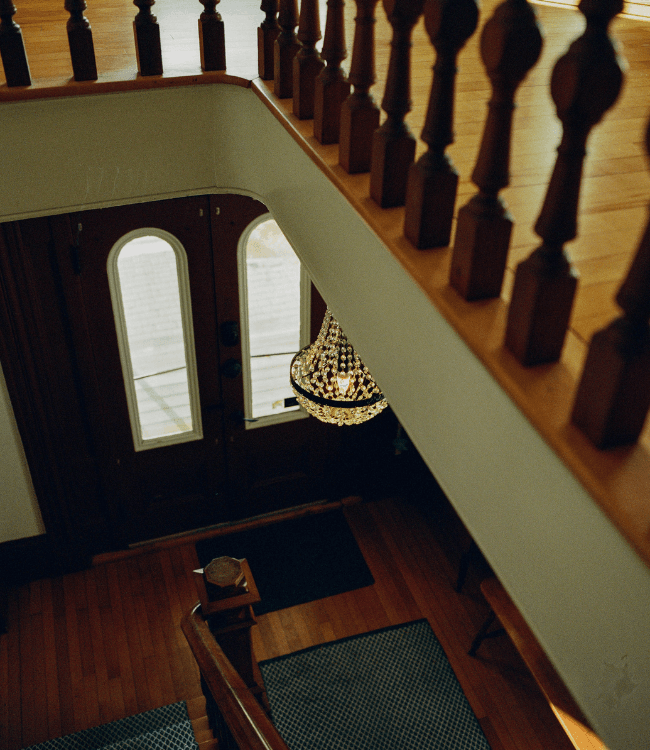 View from above a staircase featuring a chandelier and wooden railings, leading to double doors.