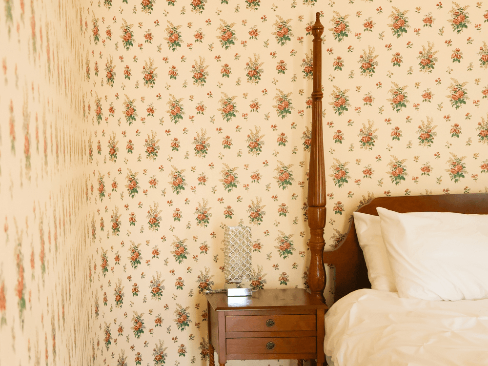 A cozy bedroom corner with floral wallpaper, a wooden bed, and a nightstand.