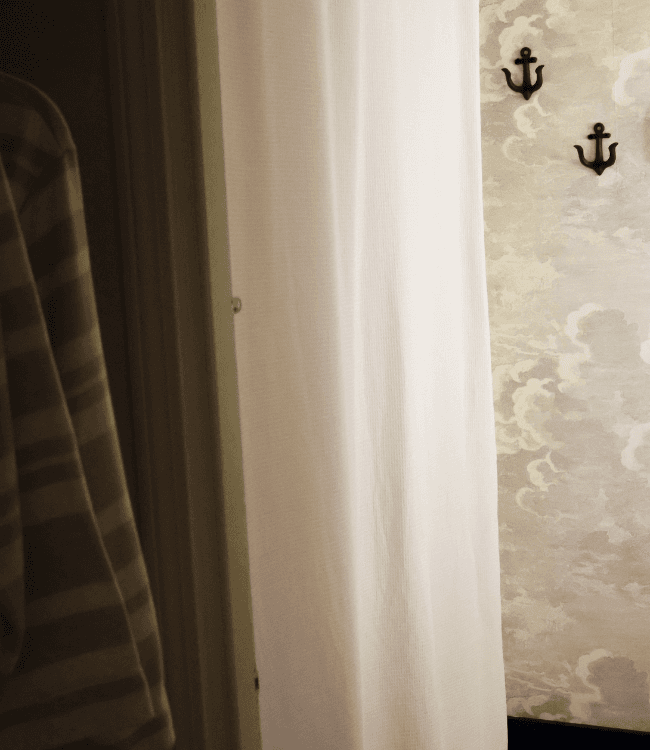 A white curtain partially obscures a doorway next to a wall decorated with a cloud pattern and two black anchors.