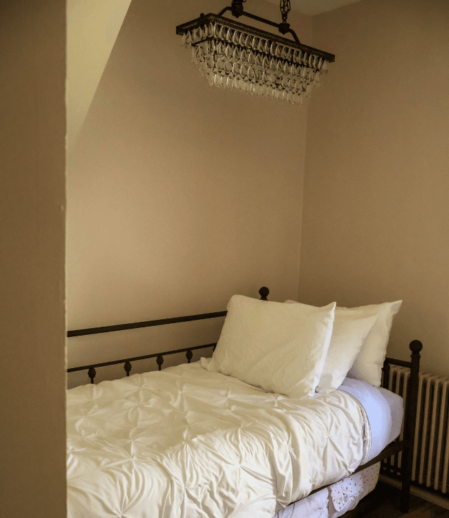 A small bedroom featuring a metal bed with white bedding and a chandelier above.