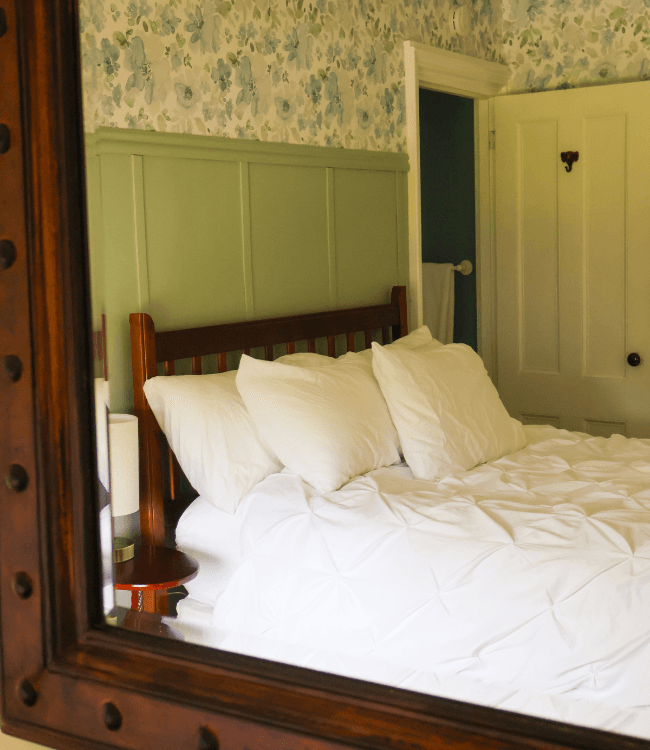 A cozy bedroom featuring a wooden bed with white linens and floral wallpaper.