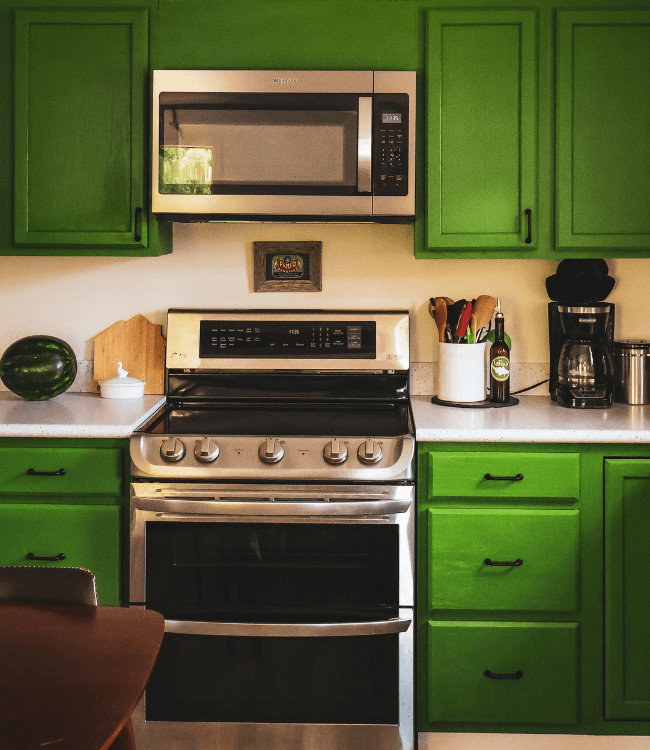 A modern kitchen featuring bright green cabinets, stainless steel appliances, and a countertop with a watermelon and utensils.