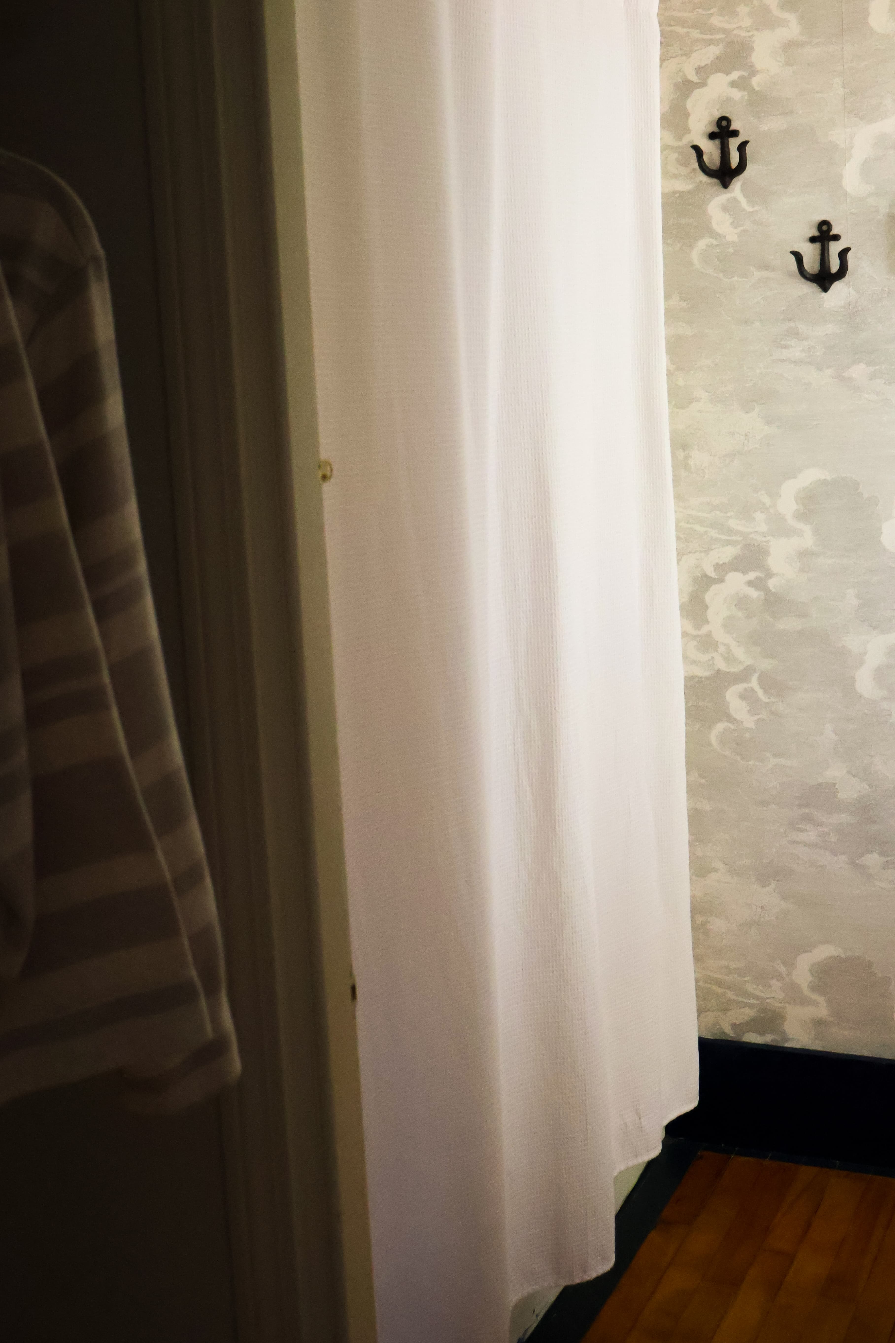 A white curtain hangs in a doorway beside two black anchor hooks against a patterned wall.