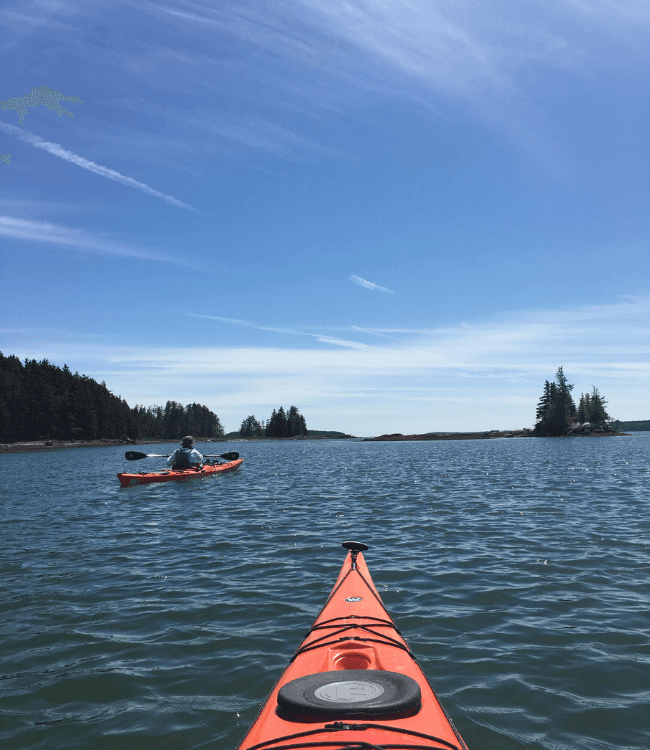 A kayak floats on calm waters with another kayaker in the distance under a clear blue sky.