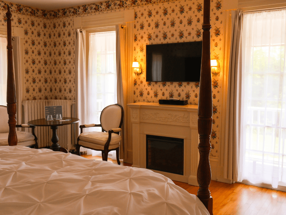 Cozy bedroom with floral wallpaper, a four-poster bed, a seating area, and a fireplace.