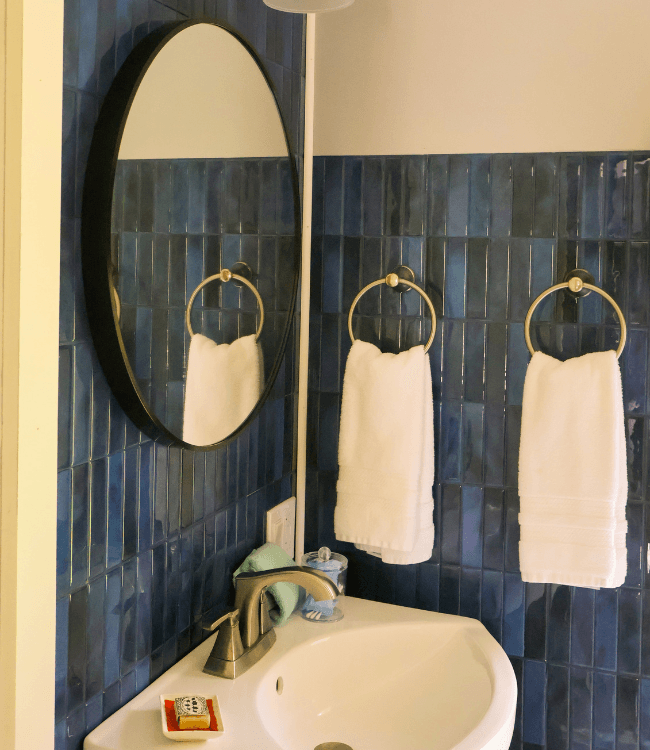 A bathroom sink area featuring a round mirror, two white towels on holders, and blue tiled walls.