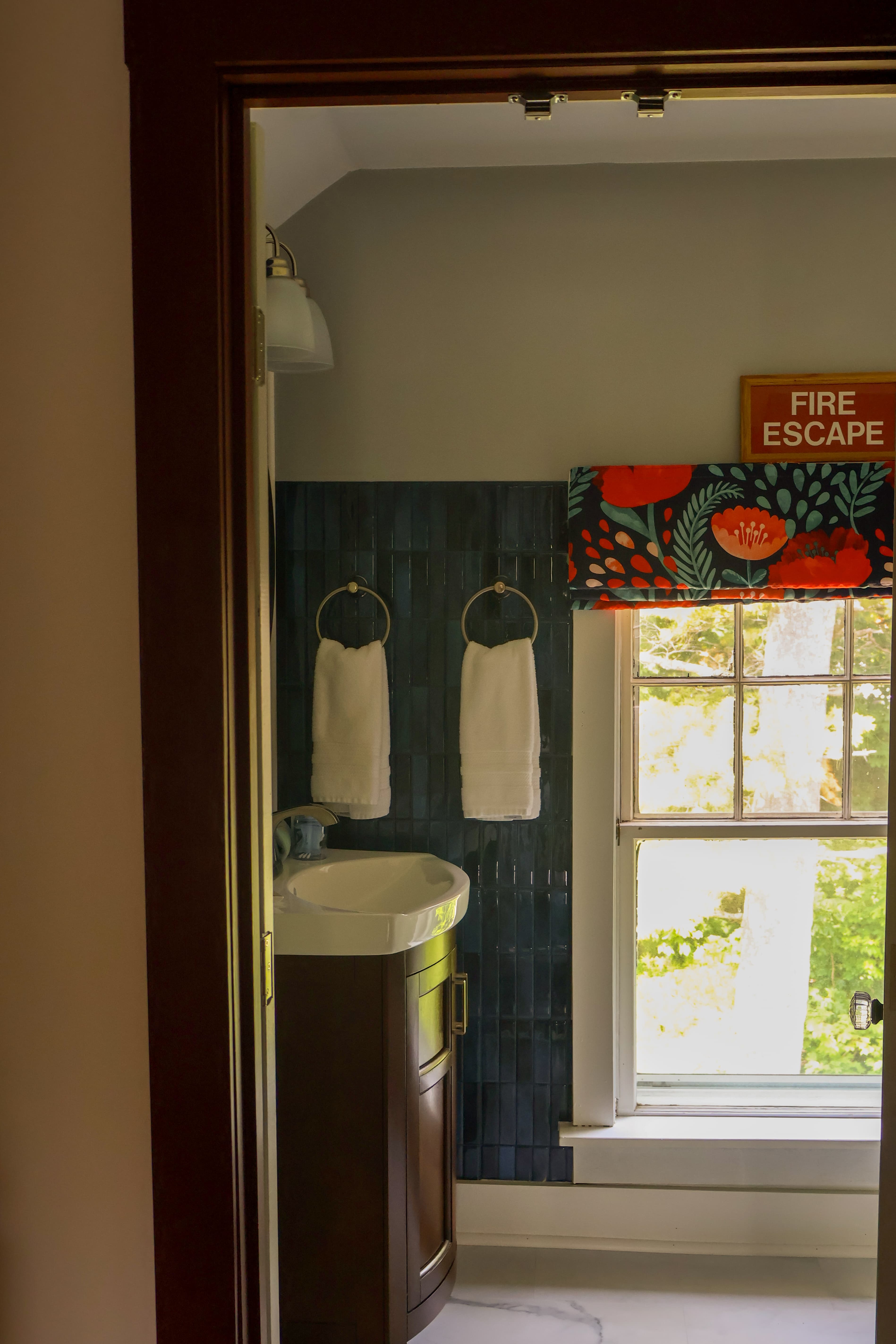View of a bathroom with a sink, hanging towels, and a window featuring a decorative curtain.